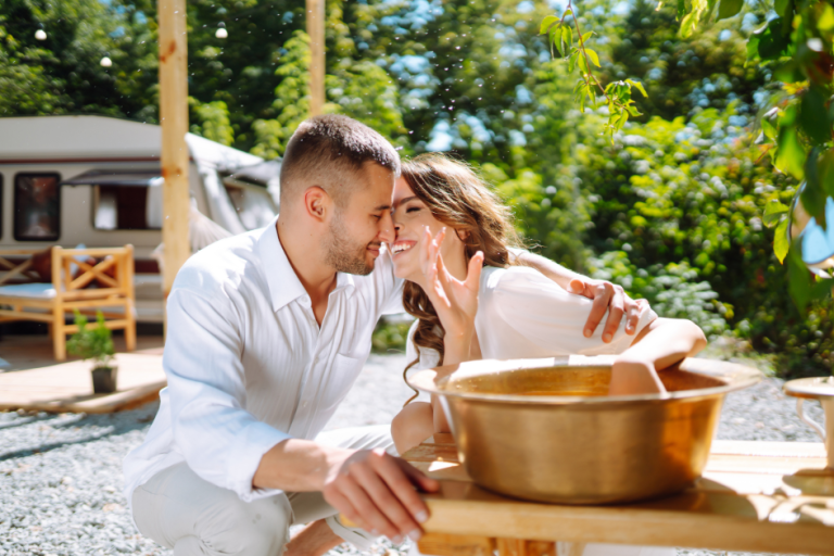 A couple cools off in a bronze bowl filled with water outside of their parked travel trailer.