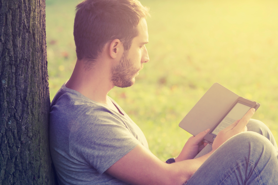 Man sits under a tree reading from an ebook