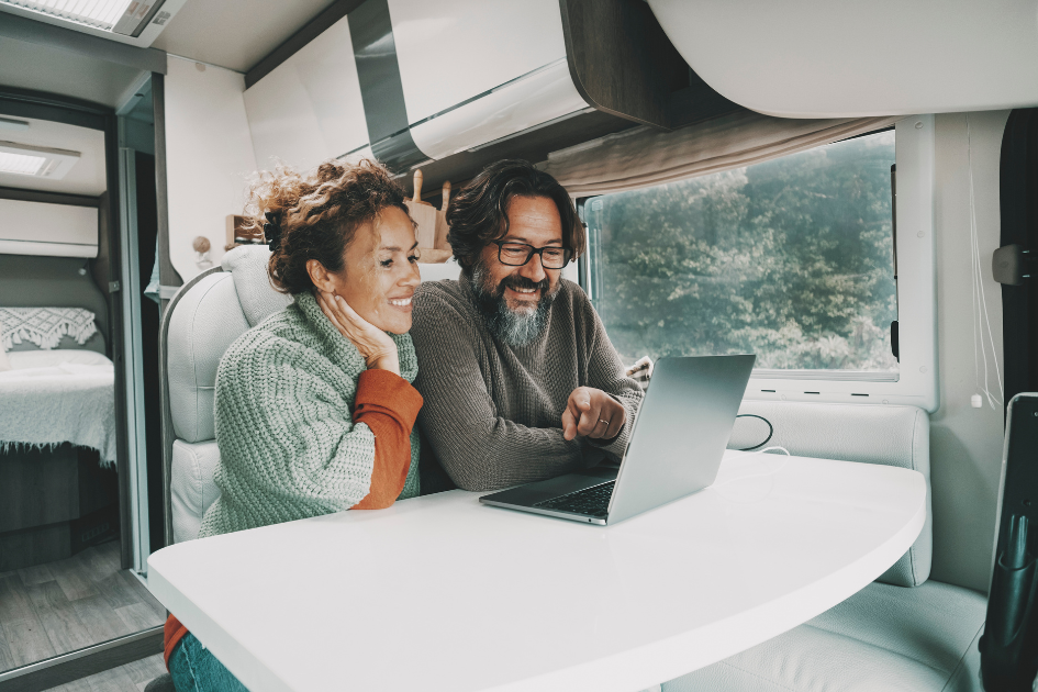 Couple sits together in their travel trailer smiling while chatting via laptop to family
