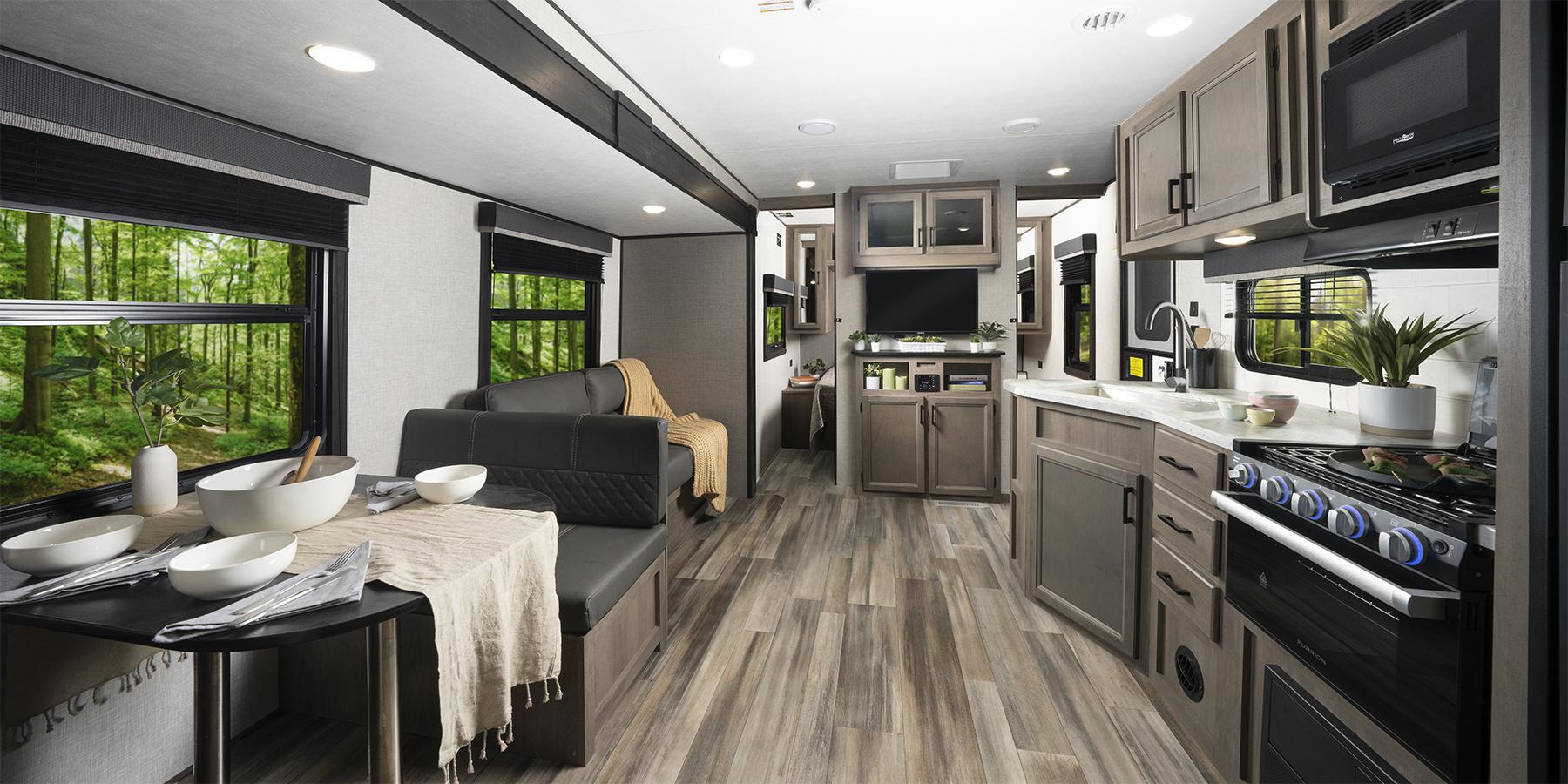 A panoramic shot of an RV's interior living area, including a spacious and beautiful kitchen, a sofa, and a dinette.